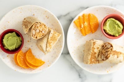 Rice and bean burritos cut in half on plates with oranges.
