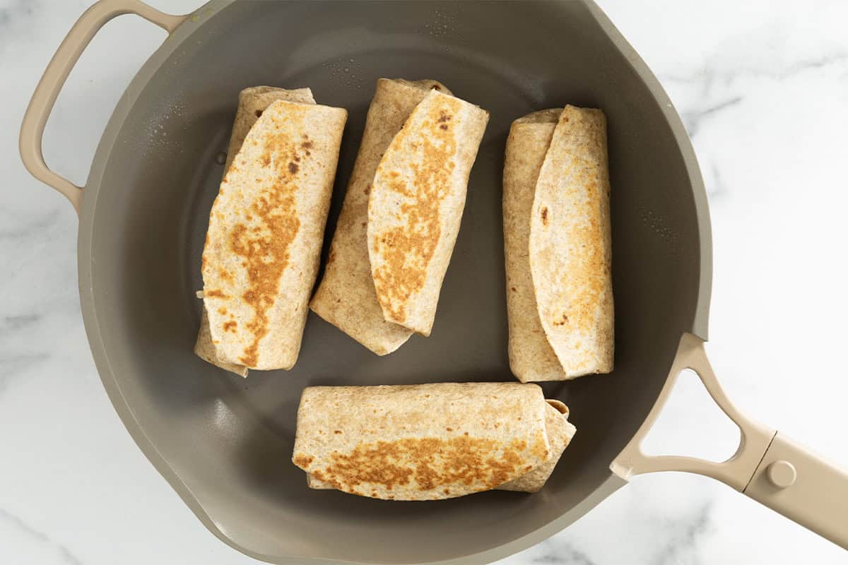 Rice and bean burritos in frying pan.
