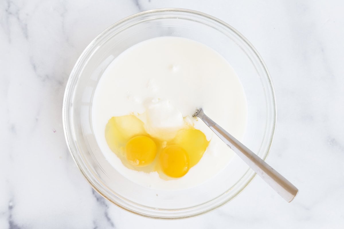 Eggs and milk in glass bowl for yogurt waffles.