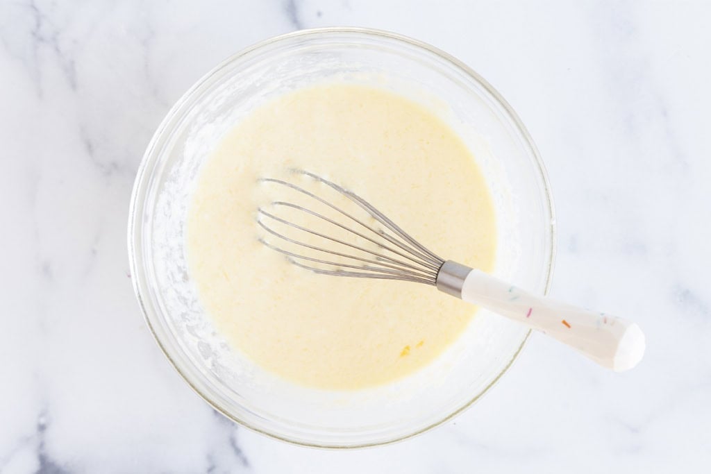 Batter for yogurt waffles in glass bowl with whisk.