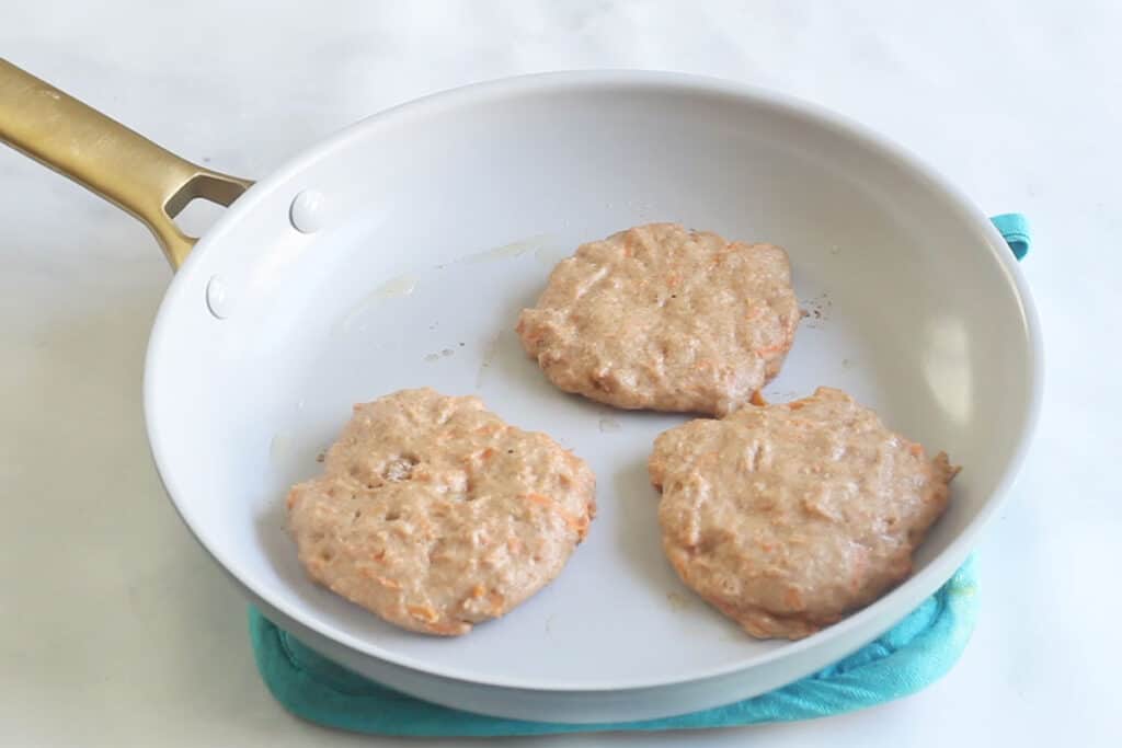cooking carrot pancakes in white ceramic pan.