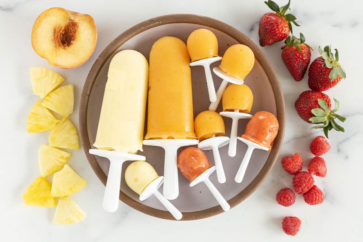fruit popsicles on plate with fruit on counter.