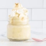 Banana pudding in glass jar with whipped cream and spoon.