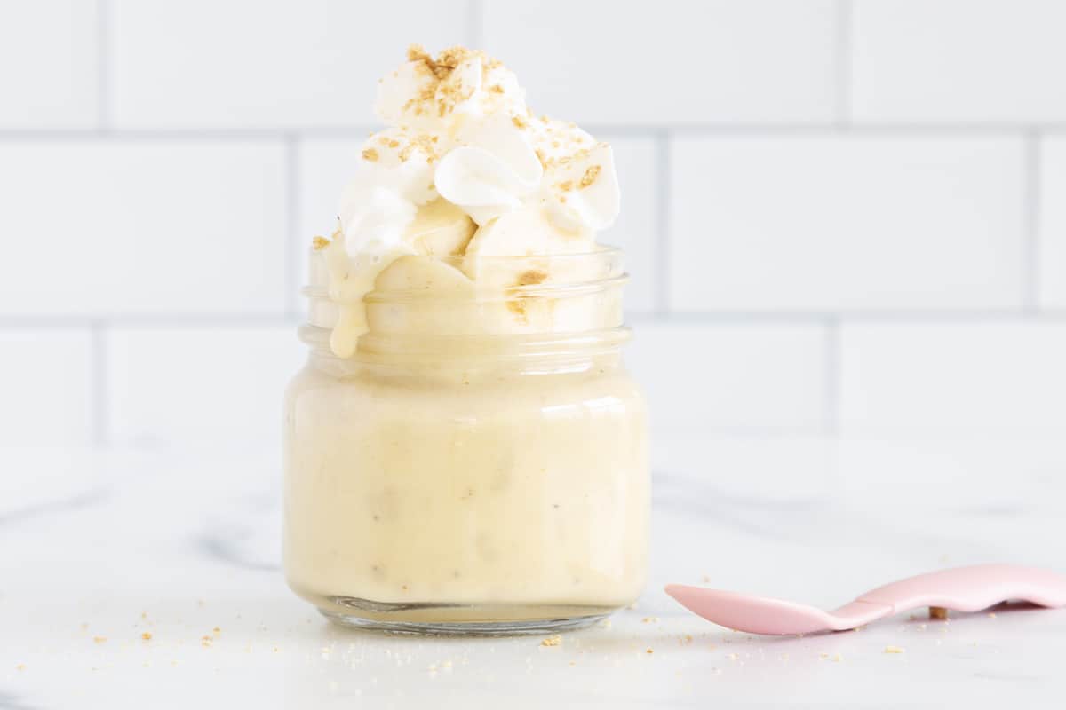 Banana pudding in glass jar with whipped cream and spoon. 