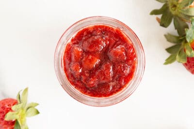 strawberry sauce in jar with berries on counter.
