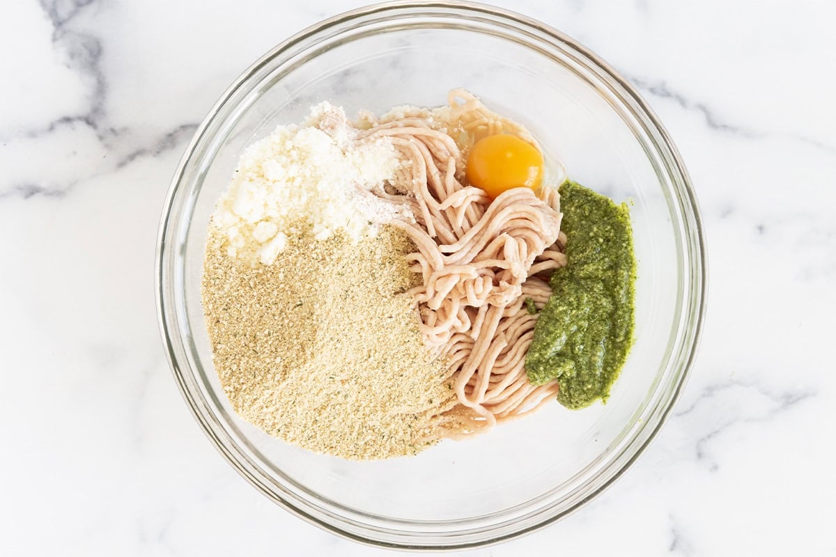 ingredients for pesto chicken meatballs in glass bowl.
