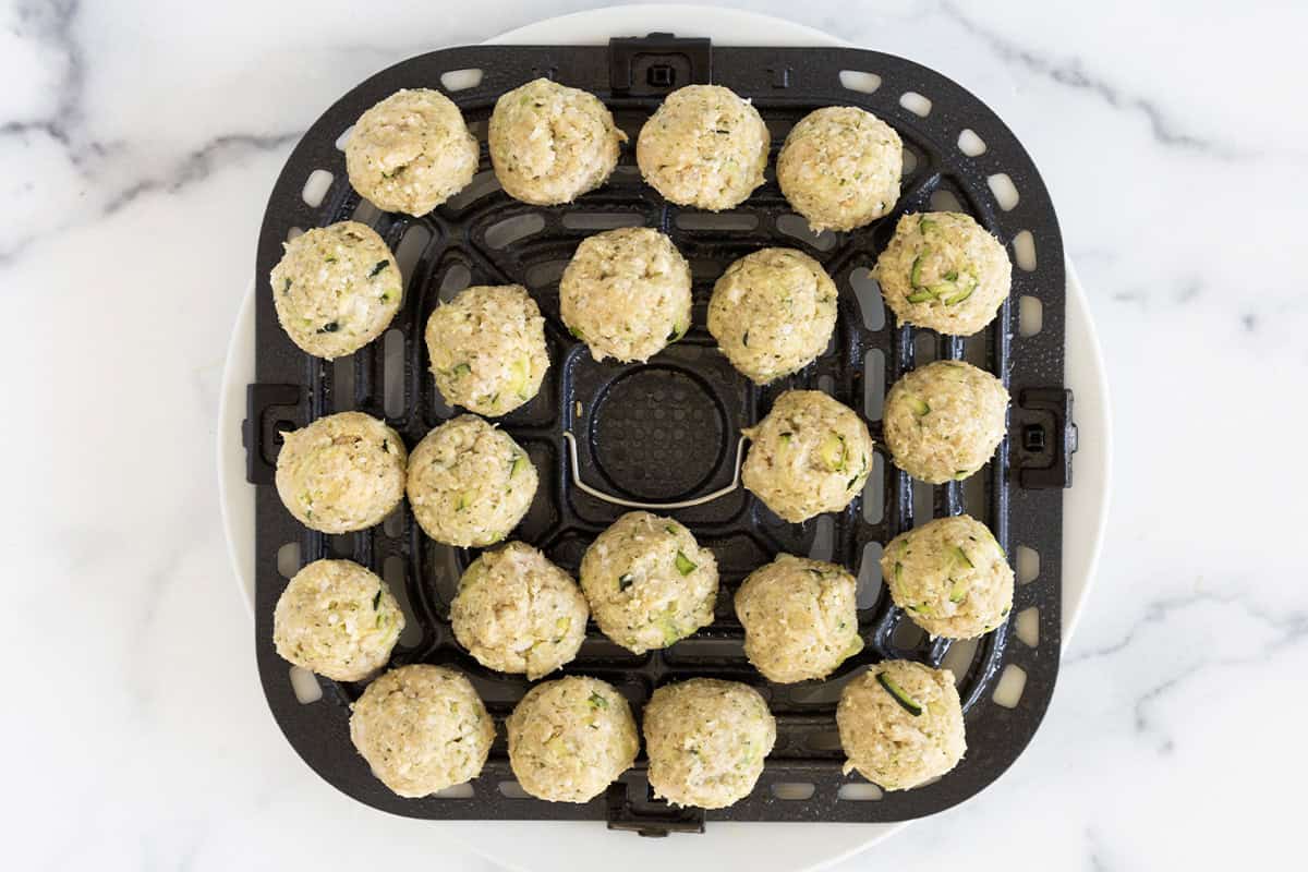 pesto meatballs on black air fryer tray.