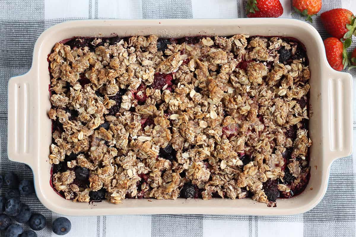 baked easy berry crisp on towel with berries.