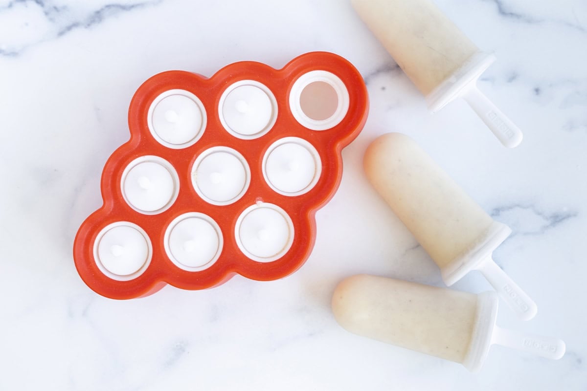 frozen banana popsicles in molds on counter.
