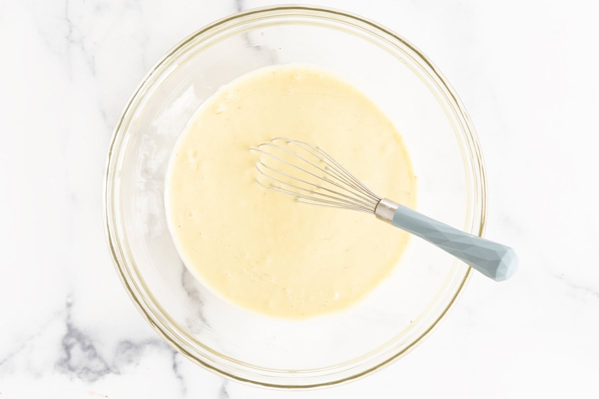 Banana pudding mixture in glass bowl with whisk.