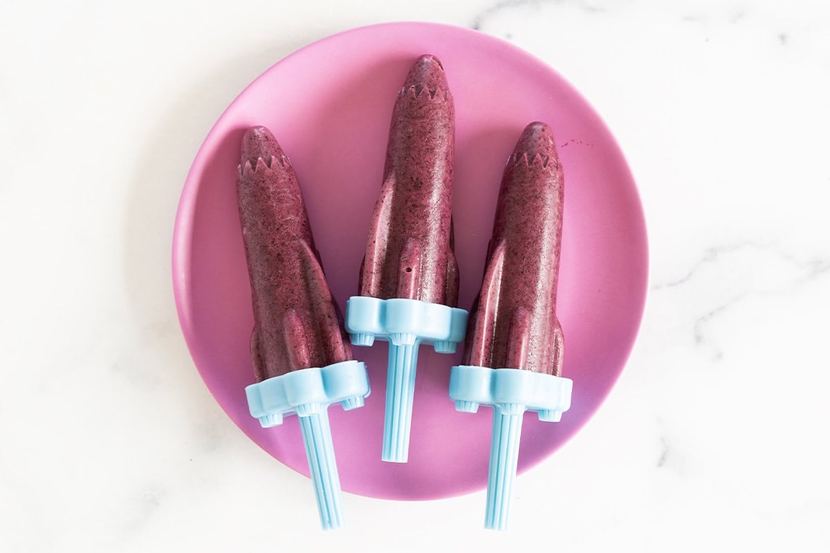 frozen blueberry popsicles on purple plate.