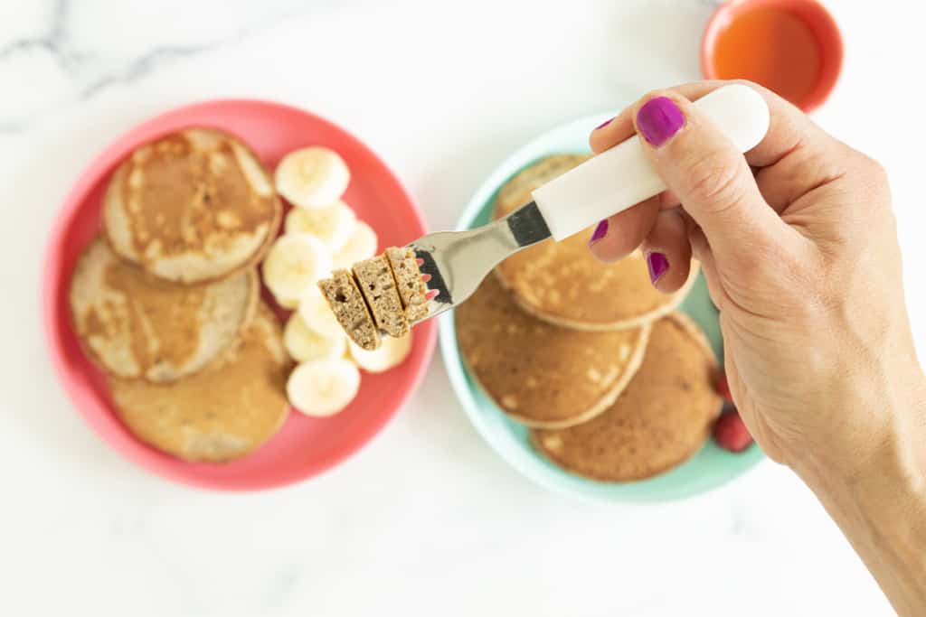 buckwheat pancakes on two plates with sides with hand holding fork.