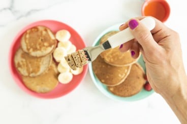 buckwheat pancakes on two plates with sides with hand holding fork.
