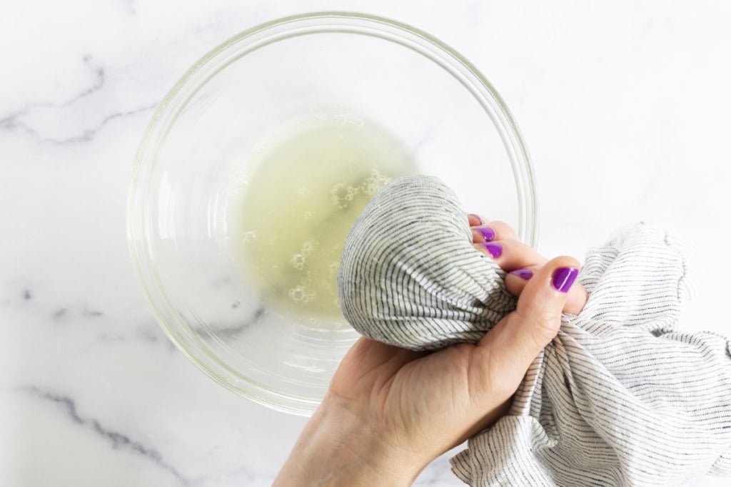 Squeezing zucchini dry for zucchini tots over glass bowl.