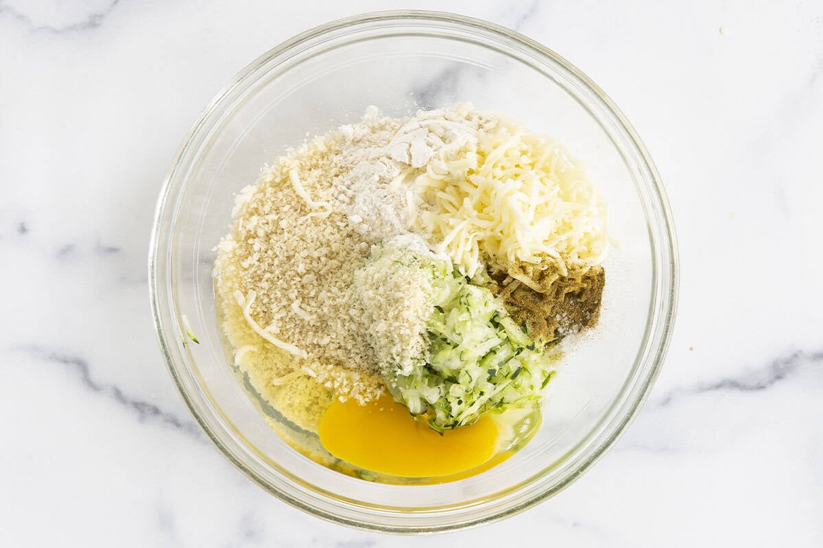 Ingredients for zucchini tots in glass bowl.