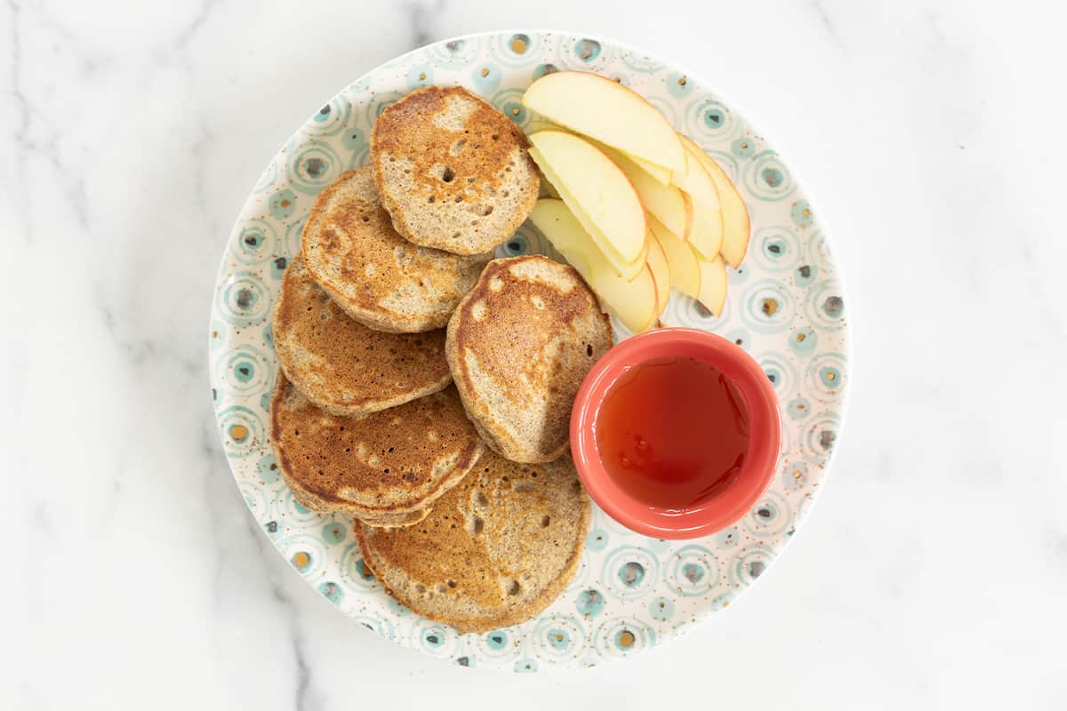 Applesauce pancakes on plate with syrup and apples.