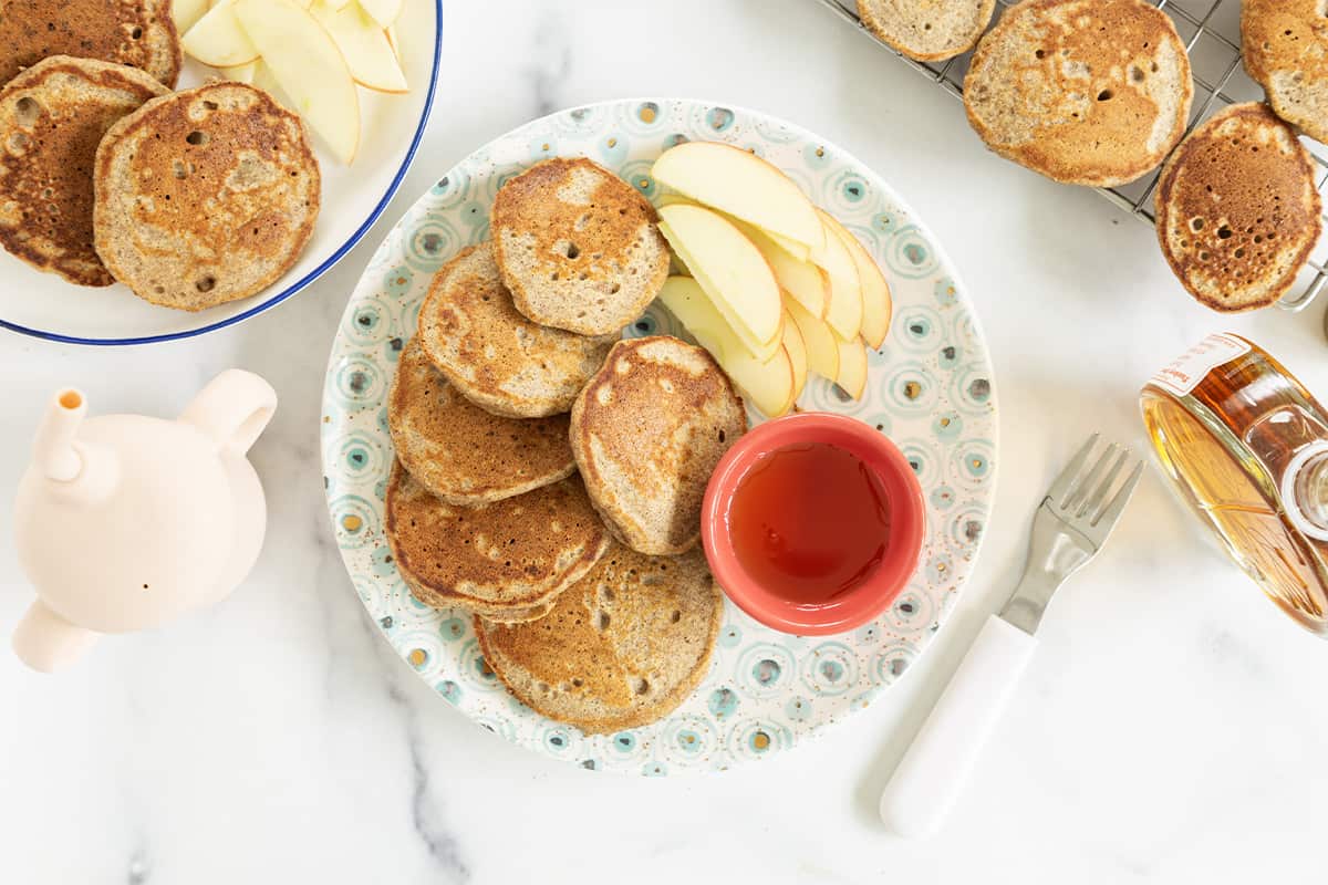 Applesauce pancakes on plate with syrup and apples. 