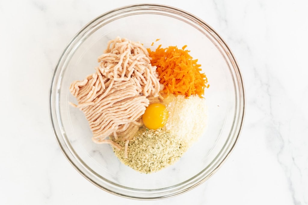 Ingredients for chicken meatballs in glass bowl before mixing.