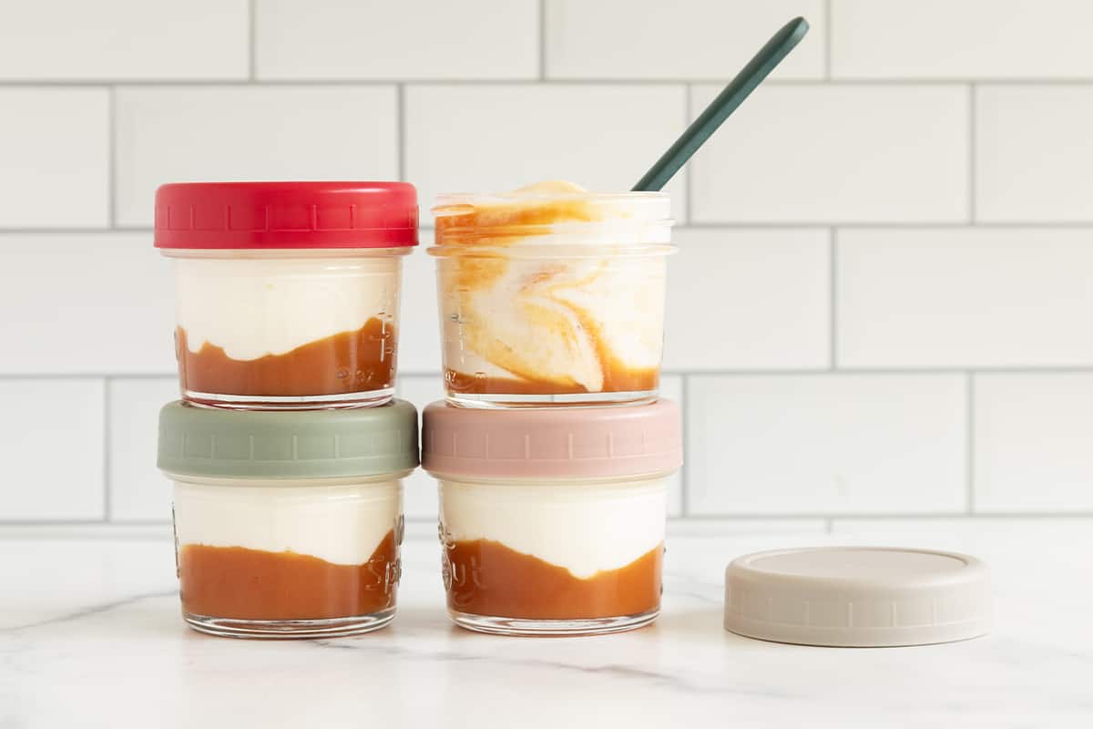 Peach yogurt in glass jars stacked on counter with spoon. 