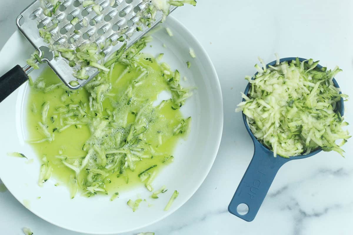 Grating zucchini into white bowl for zucchini banana bread.