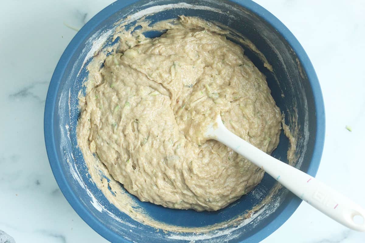 Batter for zucchini banana bread in blue bowl with spoon.