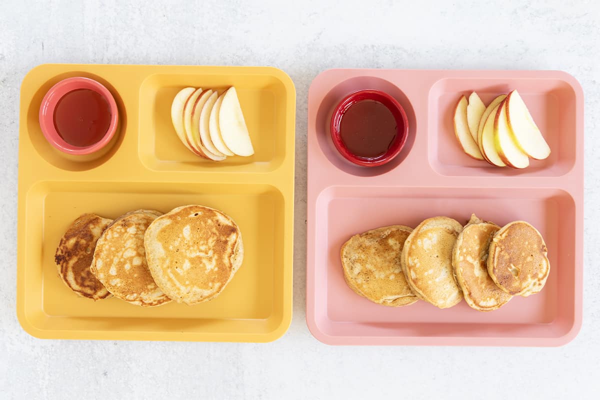 Apple cinnamon pancakes on two kids plates with sides.