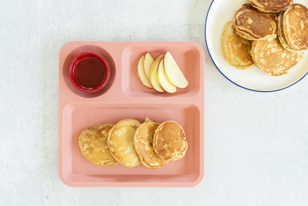 Apple cinnamon pancakes on kids pink plate with sides.