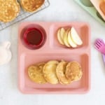 Apple cinnamon pancakes on kids pink plate with sides.
