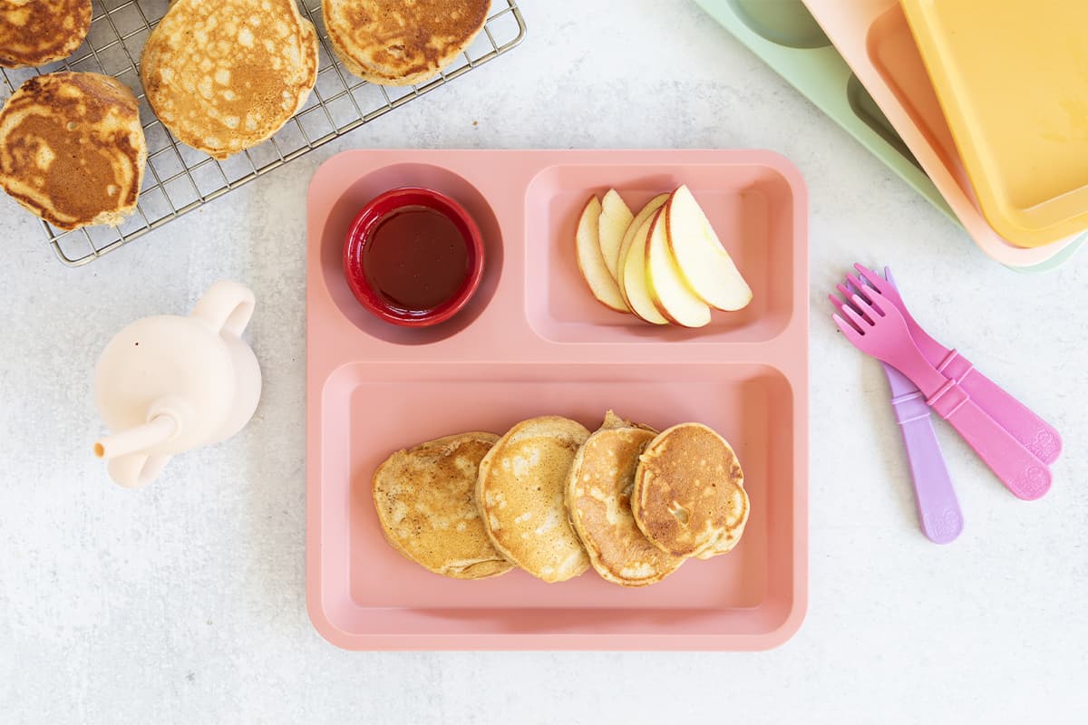 Apple cinnamon pancakes on kids pink plate with sides. 