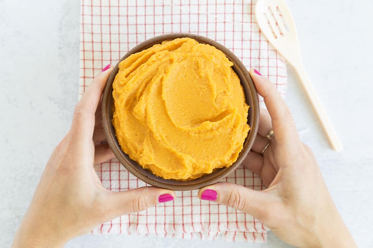 bowl of mashed sweet potatoes in bowl with hands.