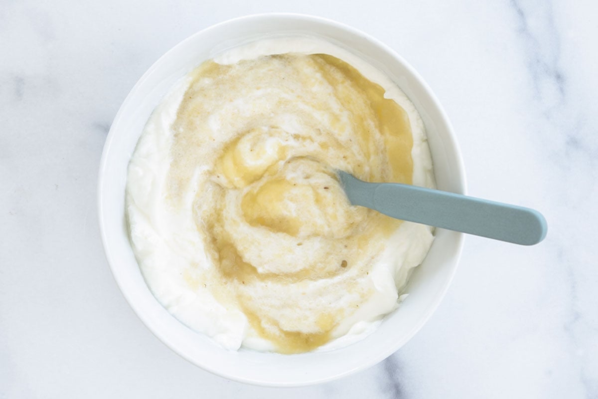 mixing yogurt and applesauce in a white bowl.