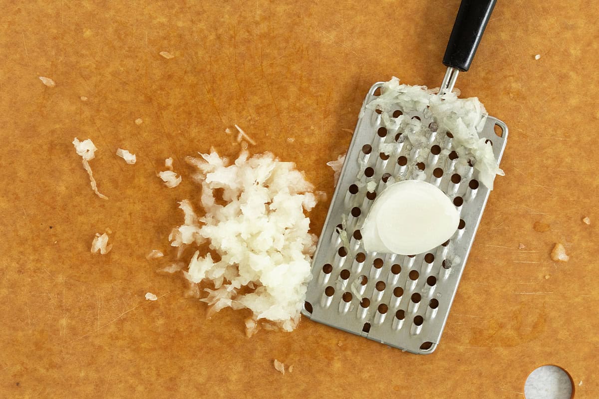 Grating onion on cutting board for orzotto with peas.