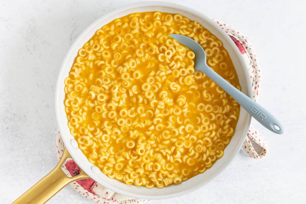 Pasta in broth in a pot with blue spoon.