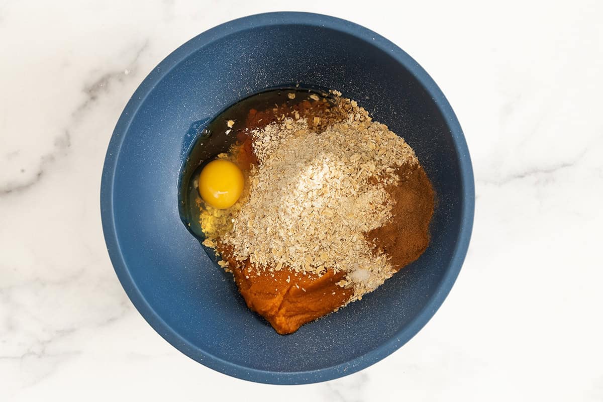 ingredients for pumpkin oatmeal cookies in blue bowl before mixing together. 