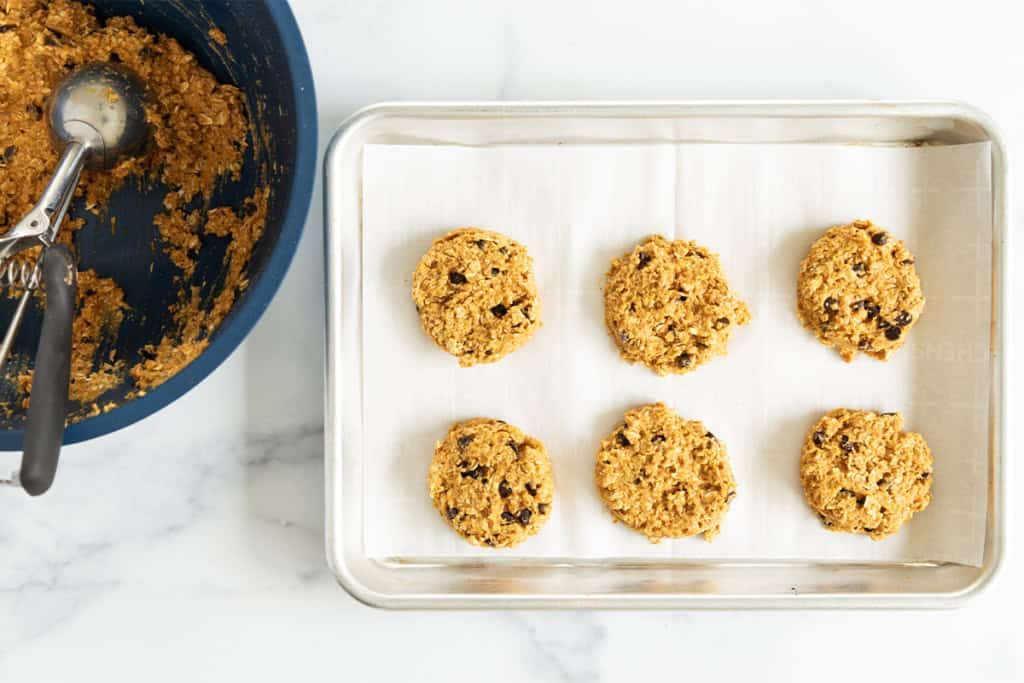 Pumpkin oatmeal cookie dough being added to baking sheet.
