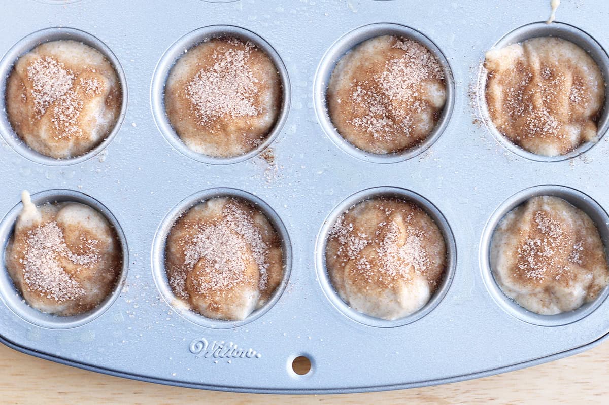 cinnamon muffin batter in pan with cinnamon sugar.
