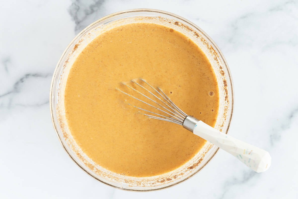Mixture for pumpkin pie in glass bowl with whisk.