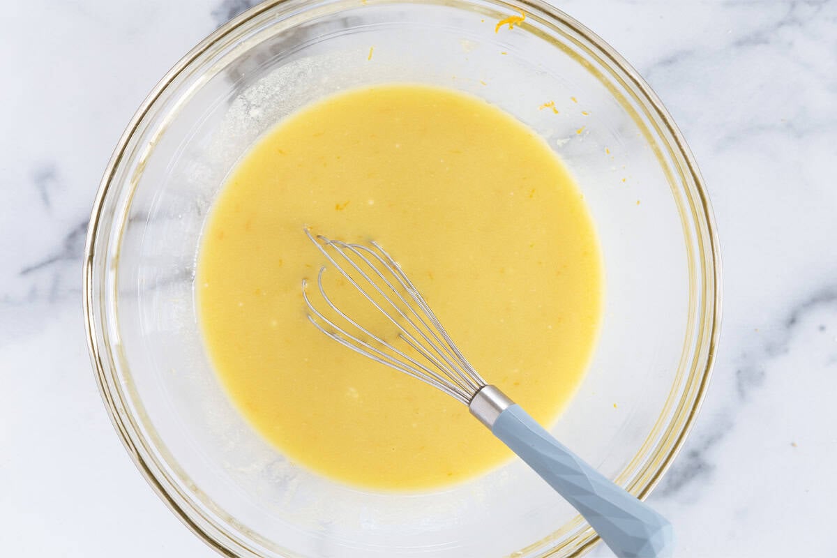 Wet ingredients for olive oil cake in glass bowl with whisk. 