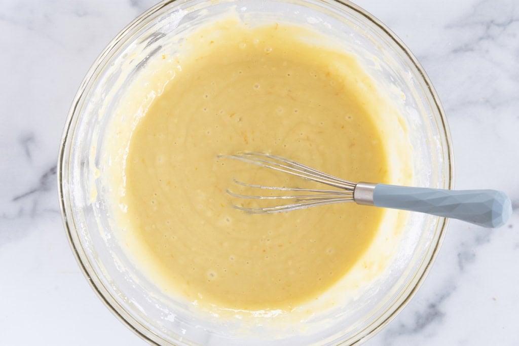 Batter for olive oil cake in glass bowl with whisk.