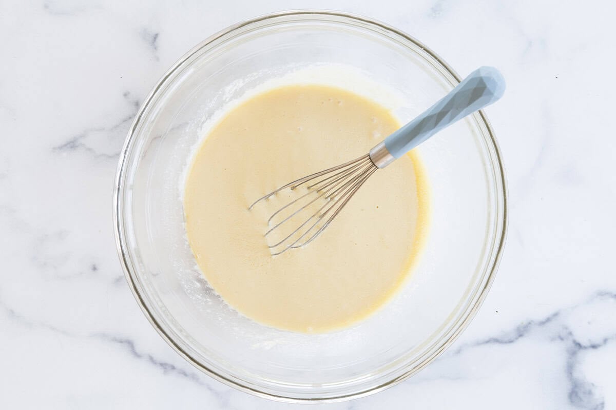 Wet ingredients for yogurt snack cake in glass bowl with whisk. 