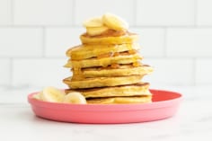 Stack of 3 ingredient banana pancakes on pink plate with syrup on top.