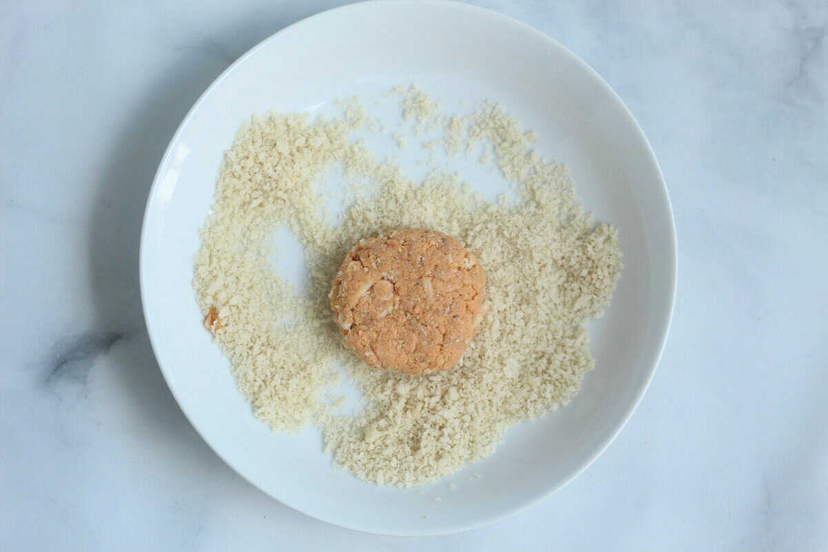 Baked salmon cake on white plate with bread crumbs.