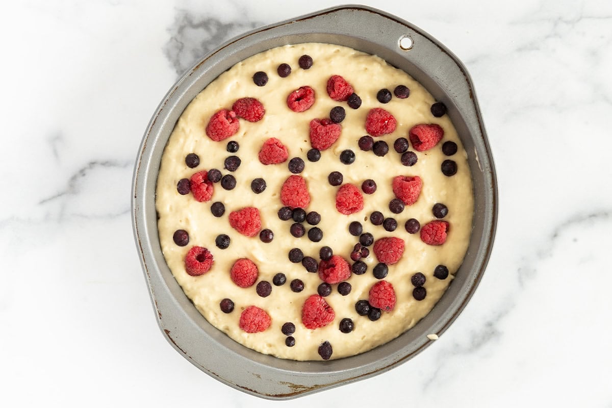 batter for breakfast cake with berries on top in pan on counter.