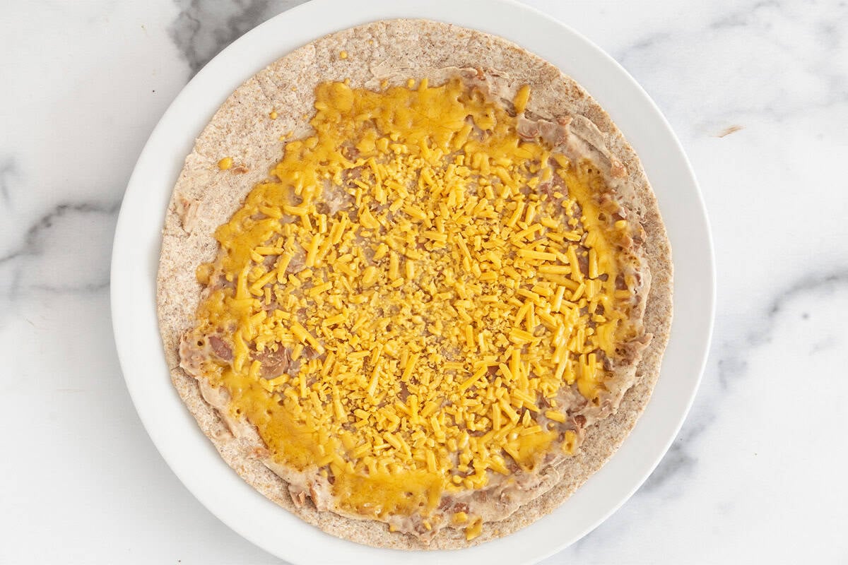 Tortilla with beans and melted cheese for taco roll ups.