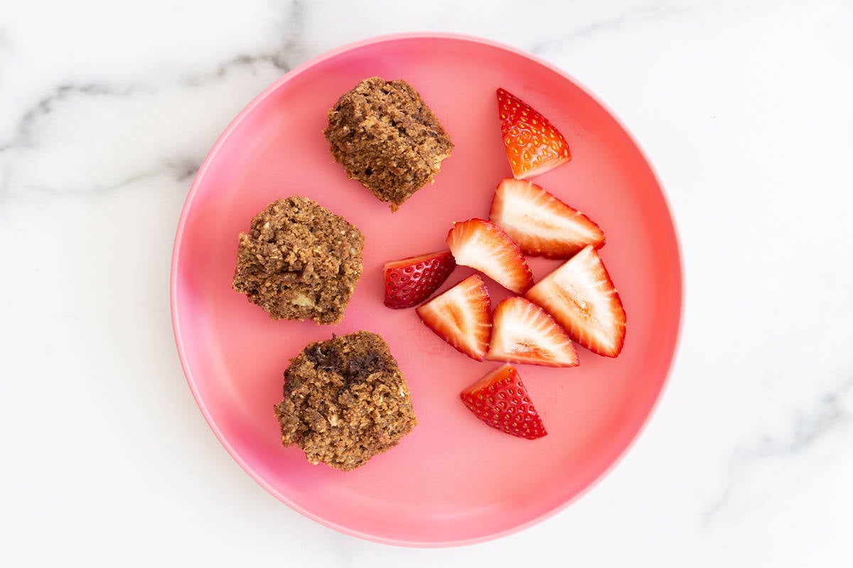 Chocolate peanut butter muffins cut into thirds on a kids plate with sliced strawberries.