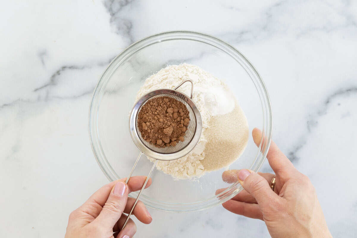 Sifting cocoa powder into glass bowl for chocolate sugar cookies.