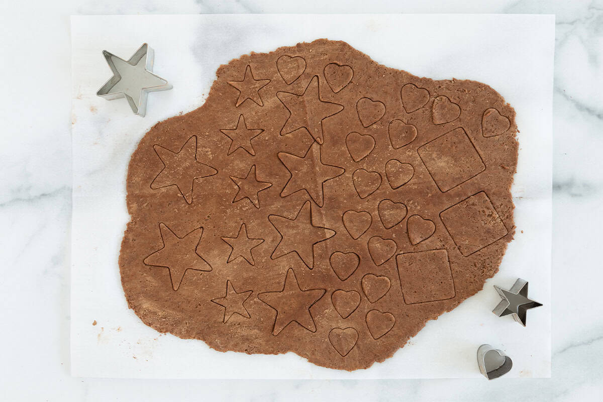 Chocolate sugar cookie dough being cut out with cookie cutters.