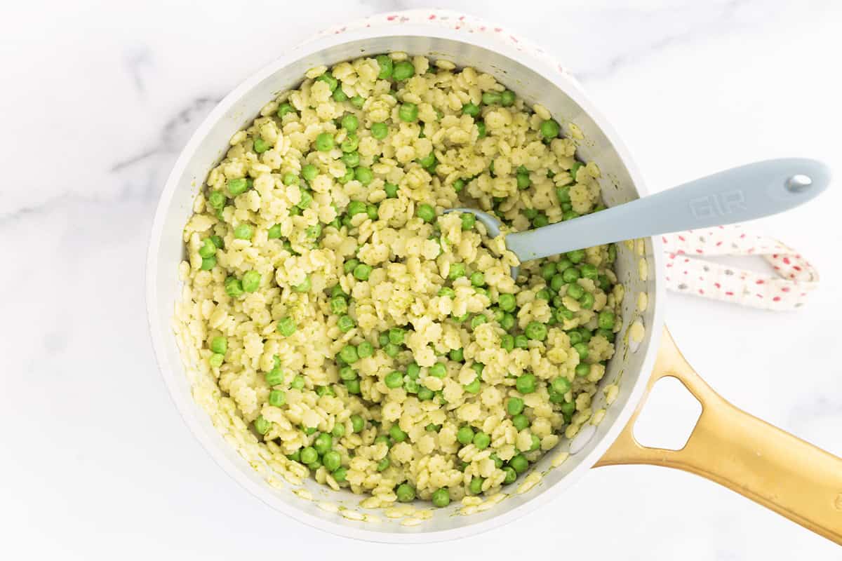 Pesto pasta with peas in pot with spoon.