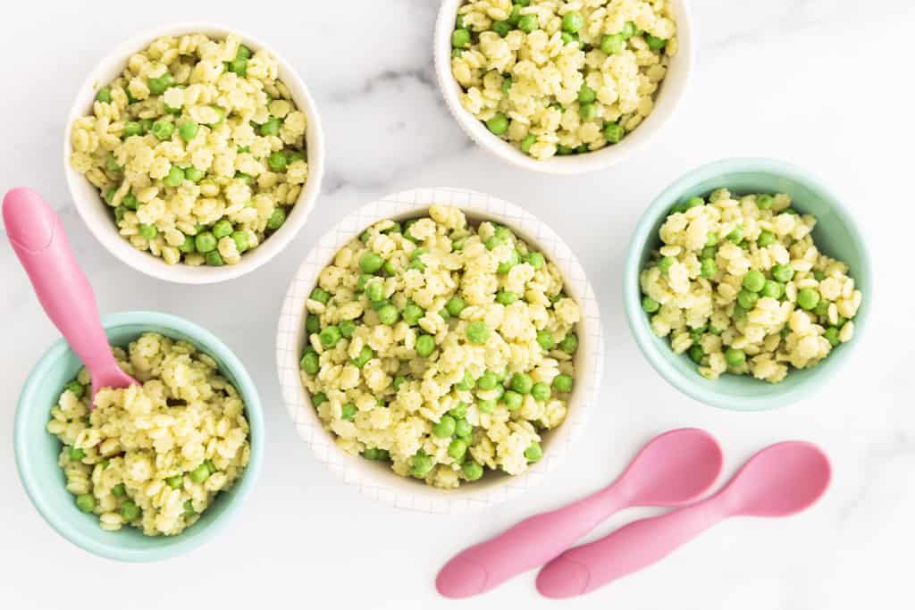 Pesto pasta with peas in five bowls with spoons.