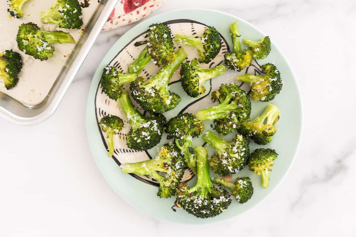 Roasted broccoli with parmesan on a plate with part of the sheet pan with more broccoli showing.